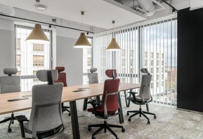 Bright meeting room with a wooden table, ergonomic chairs, and large windows with vertical blinds.