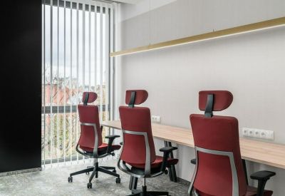 Light-filled workspace with a long wooden desk and three red ergonomic chairs.