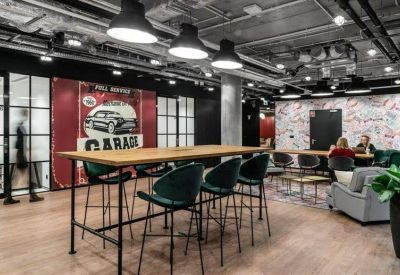 Modern coworking space with a high wooden table, teal bar stools, and industrial lighting.
