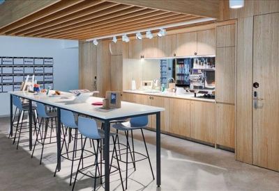 Modern breakroom kitchen with light wood cabinetry and high bar stool seating.