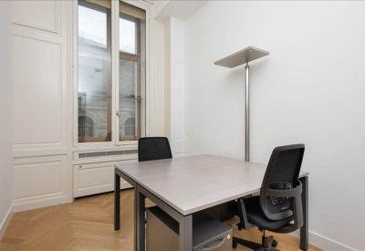 Private office space with a gray desk and black mesh chair near a tall window.