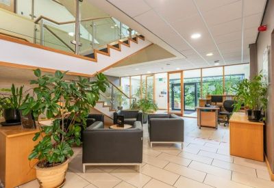 Spacious reception lobby with a wooden staircase, black leather armchairs, and indoor plants.