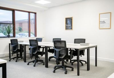 Collaborative workspace featuring long white desks and black mesh office chairs.