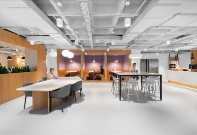 Spacious coworking lounge with high tables, grey chairs, and wood paneling.