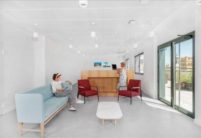 Light-filled lounge area with a blue sofa, red armchairs, and a wood reception counter.