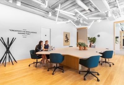 Modern coworking space featuring a large irregularly shaped wooden table and designer blue chairs.