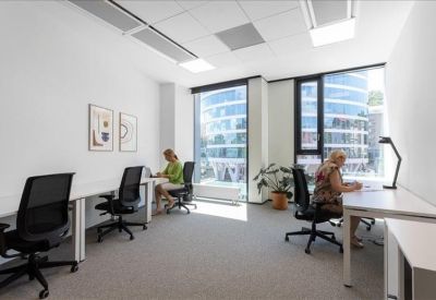 Bright four-person office suite with white desks and large windows overlooking the city.