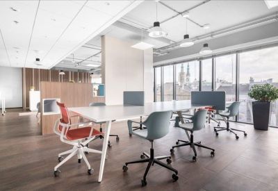 Modern coworking area with long white table, colorful chairs, and city skyline views.