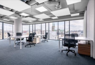 Spacious open-plan workspace with multiple desks, black ergonomic chairs, and large windows.