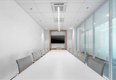 Long white boardroom table with grey mesh chairs and a wall-mounted screen.