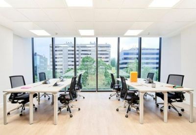 Bright open-plan office with white desks, black chairs, and floor-to-ceiling windows.