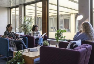Bright communal lounge with plush armchairs and residents chatting near large windows.