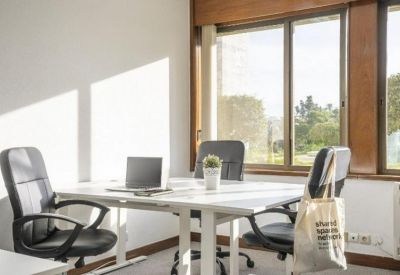 Bright shared office with white desks, ergonomic black chairs, and large windows.