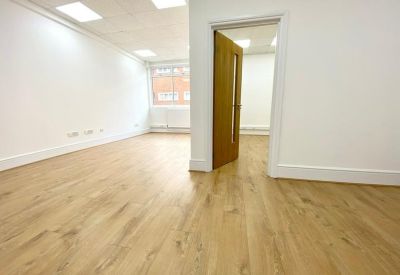 Bright, empty workspace with light wood flooring and an open doorway leading to another room.