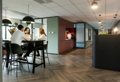 Communal break area with people sitting at a high table near a built-in kitchenette and chevron wood flooring.