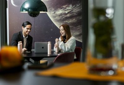 Coworking space where two people converse at a table beneath a large planet mural and green pendant lamp.