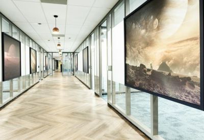 Bright glass-walled corridor lined with large framed space-themed artwork and light wood flooring.