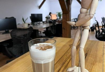 Close-up of a latte next to a wooden artist mannequin on a high timber office table.