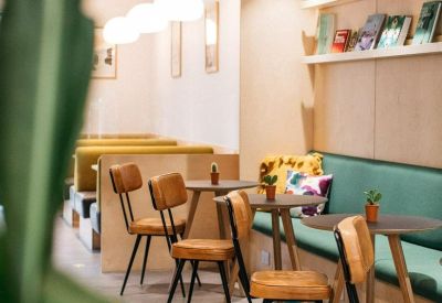 Modern café area featuring tan leather chairs, small round tables, and a teal banquette seat.