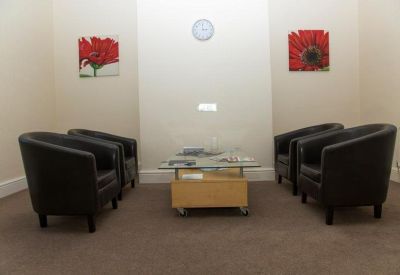 Waiting area with four black leather tub chairs and red floral wall art.