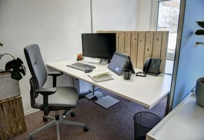 Individual workstation with a white desk, grey ergonomic chair, and wooden privacy screen.