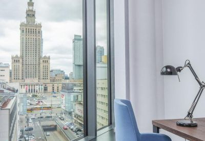 Private office workstation with a blue chair, wooden desk, and a view of the Palace of Culture and Science.