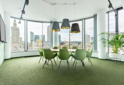 Bright boardroom with green chairs, wooden table, and panoramic windows overlooking the city skyline.