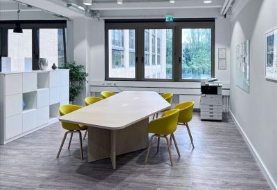 Modern office kitchen area with white cabinetry, blue backsplash, and yellow dining chairs.