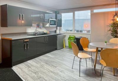 Modern communal kitchen and dining area with grey cabinetry and light wood-effect flooring.