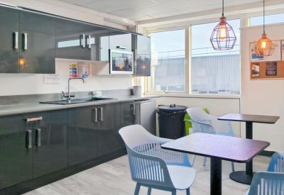 Communal kitchen area with grey cabinetry and blue chairs at dining tables.