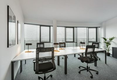 Spacious open-plan office with white desks and black ergonomic chairs by large windows.