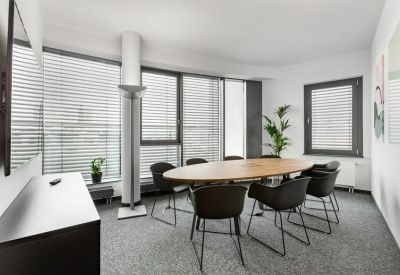 Meeting room with an oval wooden table, black chairs, and natural light from window blinds.