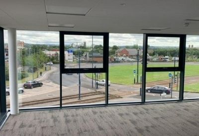 Large windows in an empty office space showing a view of the nearby street and greenery.