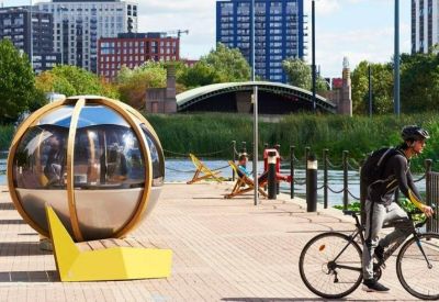 Outdoor wooden terrace by the water with a spherical seating pod and cyclist.
