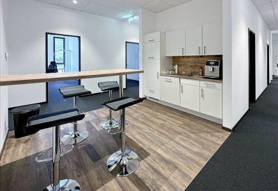 Modern communal kitchen and breakout area with high bar stools and wooden flooring.