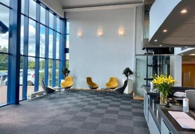 Double-height lobby area with yellow accent chairs, checkered carpet, and large glass windows.