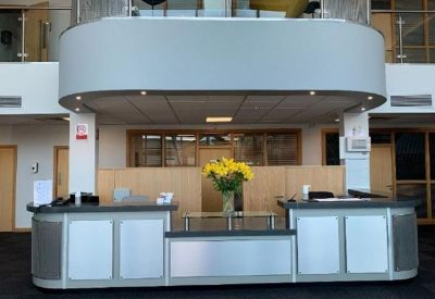 Modern grey and silver reception desk under a mezzanine level with fresh yellow flowers.