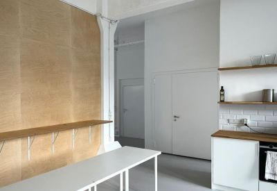 Minimalist communal area with plywood wall feature and long white tables.