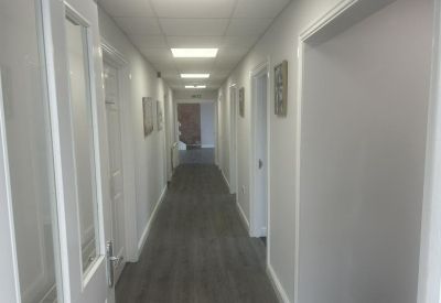 Long bright hallway with grey wood-effect flooring and multiple white doors leading to offices.