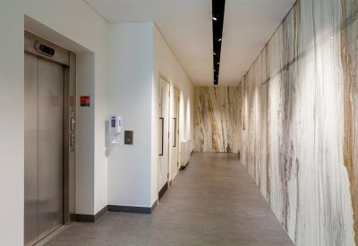 Polished corridor with marble-effect wall panels leading to an elevator and side rooms.