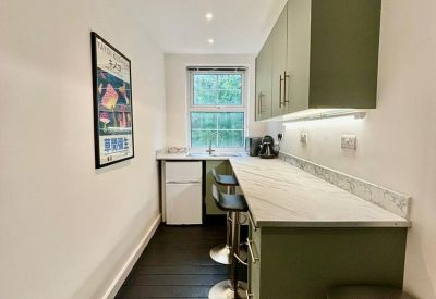 Long, narrow kitchenette with green cabinetry, marble-effect countertop, and bar stools.