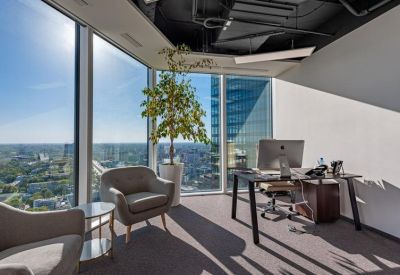 Executive corner office with panoramic floor-to-ceiling windows and a large potted tree.