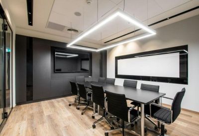 Bright conference room with a large black table, ergonomic chairs, and geometric LED lighting.