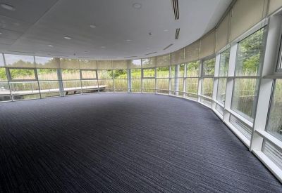 Curved open-plan workspace featuring floor-to-ceiling windows and grey carpeting.