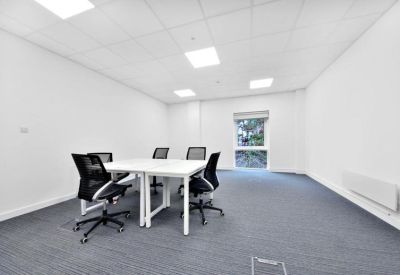 Four-person meeting room with white desks, mesh chairs, and grey carpet.