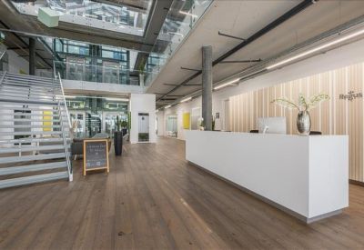 Minimalist white reception desk in a bright, open-plan lobby with wooden flooring.