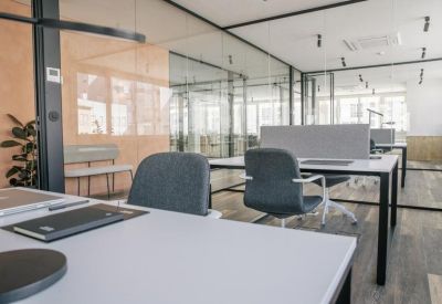 Modern open-plan workspace with glass partitions, white desks, and ergonomic grey chairs.