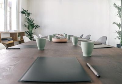 Long wooden boardroom table set with notebooks and cups, accented by indoor palm plants.