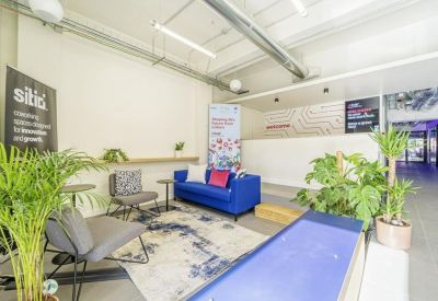 Reception area with a blue sofa, indoor plants, and a wooden shelf under industrial ceilings.