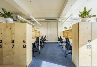 Open-plan office area with numbered wooden lockers and black ergonomic mesh chairs.